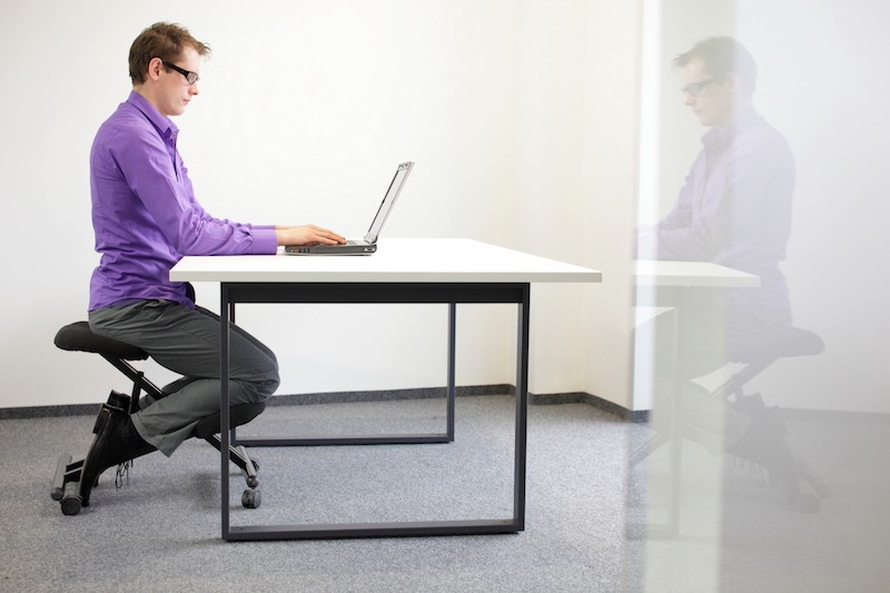 Man using saddle chair while working in office