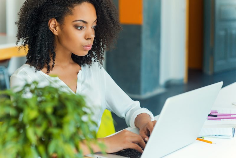 African-American lady working on a white laptop concentrating on her tasks