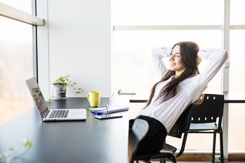 Young lady stretching while sitting at a minimal desk in front of a laptop computer